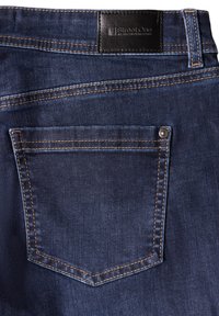 Mörkblå denimjeans med en bakficka med dubbelsömmar och en silverfärgad tryckknapp. Midjan har en svart läderetikett.