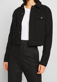 Černá zkrácená denimová bunda s knoflíkovým zapínáním, dvěma předními kapsami a klasickým límcem. Obsahuje hladkou, texturovanou tkaninu.