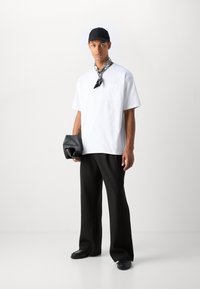 Vit t-shirt med kort ärm och ficka, svarta vida byxor, svart keps, svart scarf och en clutchväska i en mjuk textur. Svarta loafers fulländar looken.