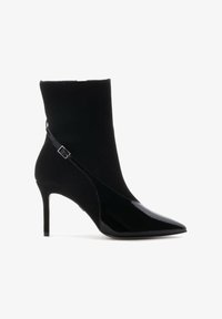 Botín negro hasta el tobillo con parte superior de ante y puntera puntiaguda de charol. Cuenta con un tacón de aguja delgado y una correa ajustable en el tobillo.