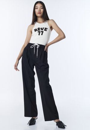 Haut blanc sans manches avec lettrage en perles noires "REVE 77", associé à un pantalon noir taille haute et des chaussures noires à brides.