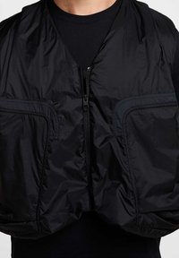 Sort nylon vest med lynlås foran, to sidelommer og en letvægts, let blank tekstur, der har en afslappet pasform og minimalt design.