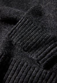 Svart stickad tyg som visar ribbat mönster med varierande mönster; mjukt ullmaterial, något fluffigt utseende med fina detaljer.