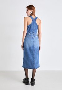 Jeansowa sukienka o bezrękawnikowym kroju, dopasowanej górze i długiej spódnicy. Jasnoniebieski kolor z delikatnym wyblaknięciem. Noszona z czarnymi, masywnymi butami.