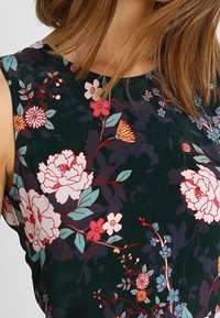 Abito floreale con uno sfondo verde scuro e motivi di peonie e piccoli fiori in rosa, bianco e blu. Tessuto morbido, design senza maniche.
