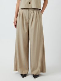Beige vide bukser med plisseringer, lavet af glat stof. Matchet med spidse sorte hæle, som har et skræddersyet og struktureret design.