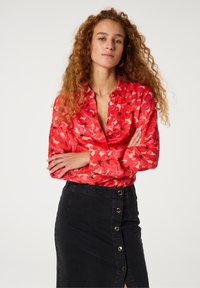 Rode bloemen blouse met lange mouwen, een kraag en knoopsluiting, gecombineerd met een zwarte denim rok met een zij-button ontwerp.