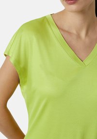 Koszulka z dekoltem w serek w jasnym limonkowym kolorze, wykonana z miękkiego, gładkiego materiału. Posiada krótkie rękawy i luźny krój, z minimalnymi detalami szycia.