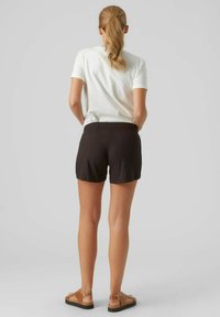 Sorte ribbede shorts med en afslappet pasform, parret med en hvid t-shirt. Shortsene har et elastisk taljebånd og bæres med brune flade sandaler.