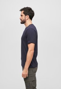 Námořnická modrá bavlněná tričko s krátkými rukávy a kulatým výstřihem, vypasovaný střih, zobrazené na muži v profilu na neutrálním pozadí.