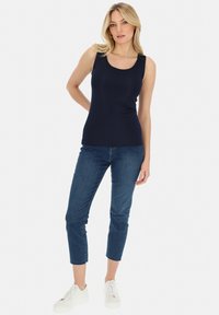 Granatowy top bez rękawów z dekoltem w łódkę i dopasowanym krojem, w połączeniu z krótkimi niebieskimi dżinsami i białymi sneakersami na neutralnym tle.