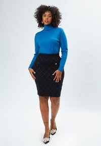 Blauer Rollkragenpullover kombiniert mit einem enganliegenden schwarzen Rock mit einem Diamantmuster und goldenen Akzenten. Schwarze Schuhe mit Perlendetails.