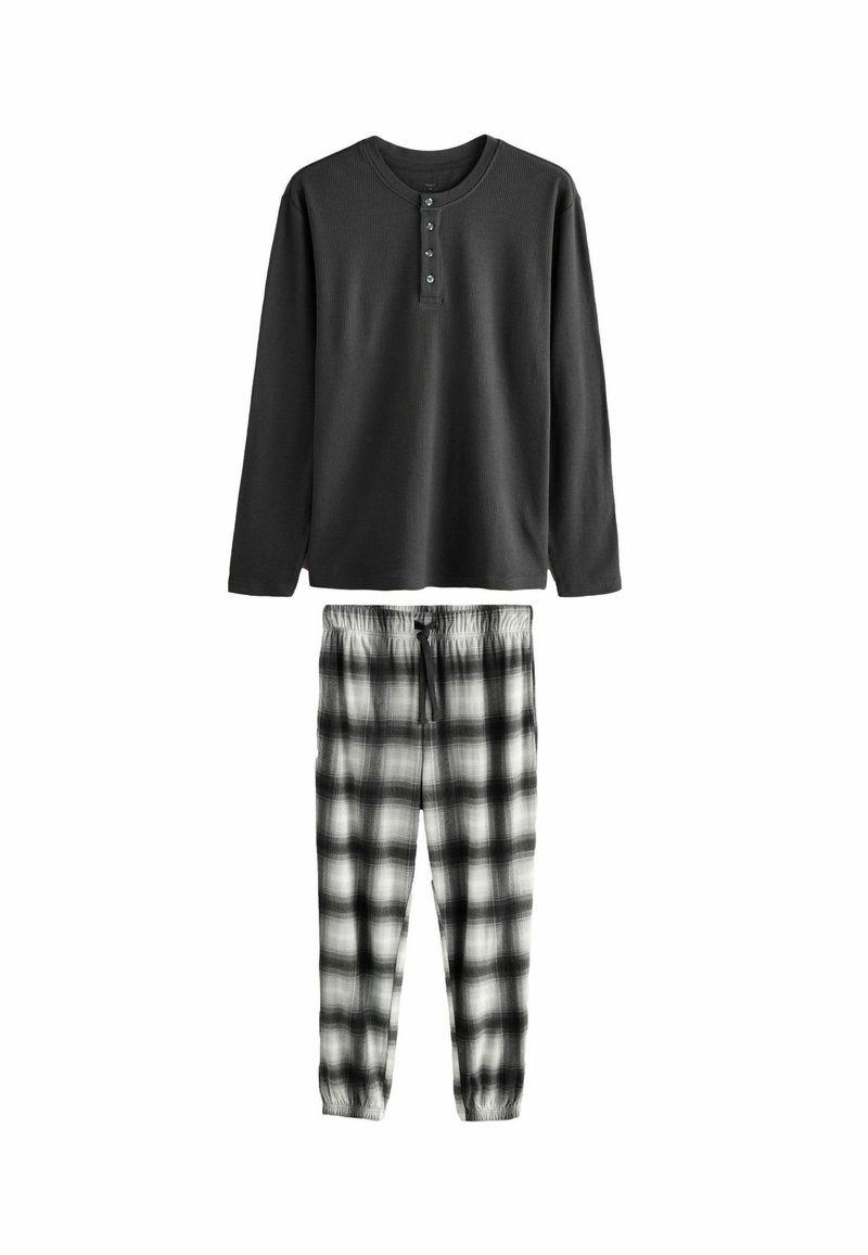 Czarna longsleeve henley z trzema guzikami, zestawiona z spodniami w czarno-białą kratę i elastycznym pasem. Miękka tekstura materiału.