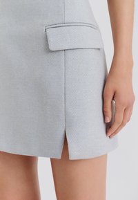 Gaiši zils svārks ar zivju kaulu rakstu, ar sānu šķēlumu un nelielu salocītu kabatas detaļu uz jostasvietas.