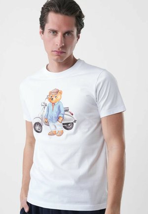 Giovane uomo con indosso una t-shirt bianca con una grafica di un orso vestito con abiti casual che sta accanto a un classico scooter.