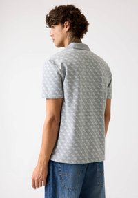 Polo gri cu mânecă scurtă, având un model subtil repetat, cu o textură netedă și un guler clasic. Asortat cu șorturi din denim albastre.