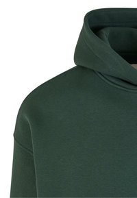 Hanorac verde închis, cu o textură moale, guler înalt căptușit și un design lejer. Detaliu de coasere vizibil la cusătura umărului.