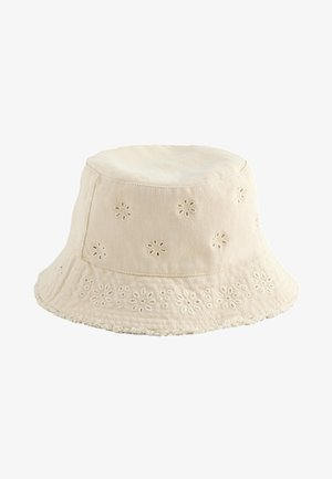 Beige stofspandhat med broderede blomsterudskårne mønstre og en frynset kant.