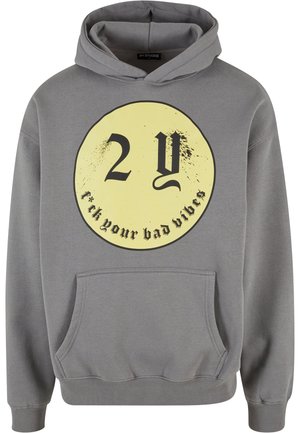 Huppari harmaasta kankaasta, jossa on etutasku ja iso pyöreä keltainen graafinen printti, jossa lukee "2Y" ja "f*ck your bad vibes" mustalla.