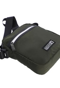 Bolso cruzado de color verde oliva hecho de tela suave. Presenta un bolsillo con cremallera blanca, detalles en negro y una correa ajustable. Logo exhibido de manera prominente.