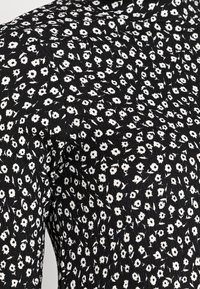 Tela negra con un pequeño estampado de flores blancas, texturizada con costuras fruncidas alrededor del hombro y la parte superior de la manga.