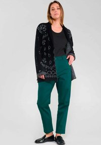 Black cardigan with white patterns, black top, green straight-leg pants, and black loafers; varied textures and colors highlighted.