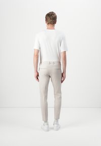T-shirt blanche ajustée et pantalon beige clair sur mesure avec une texture lisse. Des baskets blanches complètent le look. Aucun logo ou motif visible.