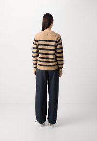 Pulover striped bej și bleumarin cu mâneci lungi, margine ribbed și detalii cu butoane pe spate, asortat cu pantaloni bleumarin cu croi lejer.