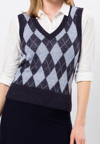 V-hals argyle vest in marineblauw en lichtblauw, gemaakt van geweven breiwerk. Gecombineerd met een witte overhemd met kraag eronder.
