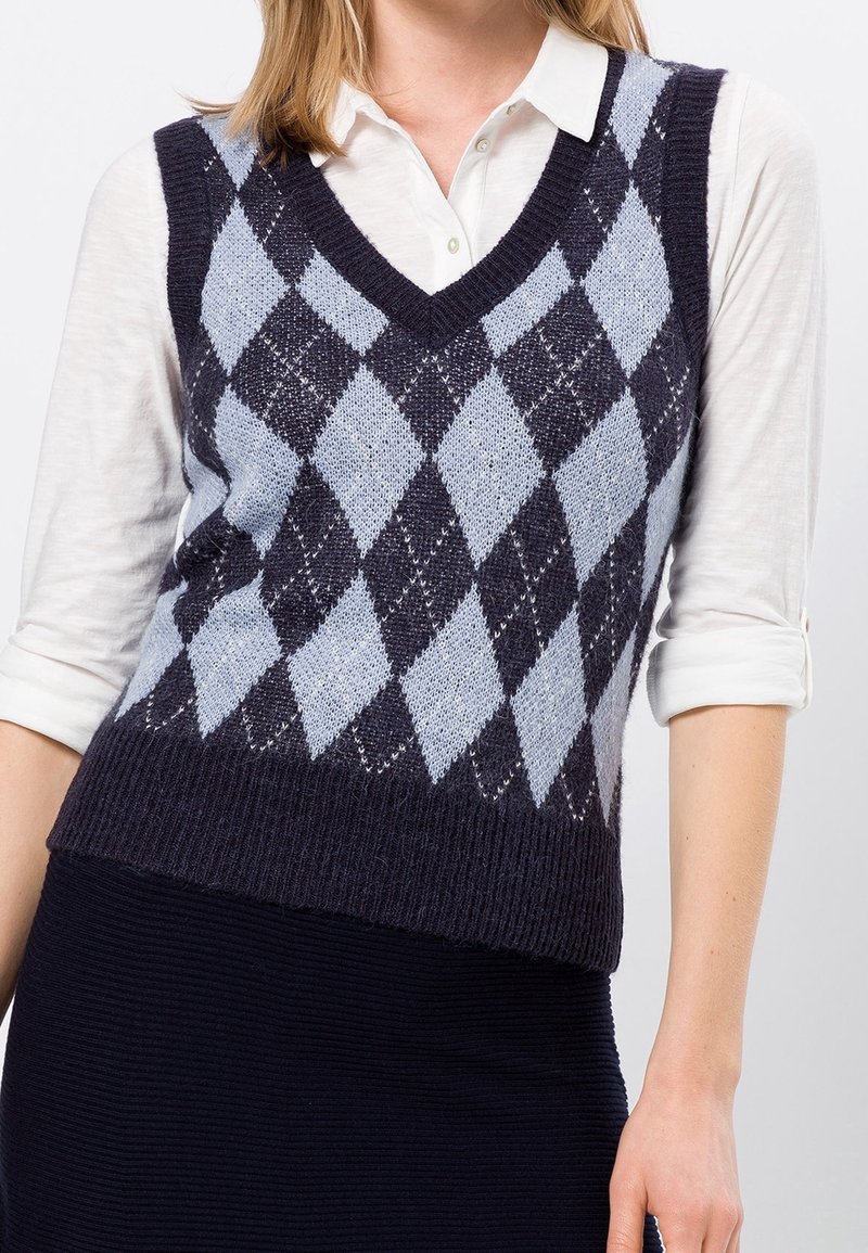 V-hals argyle vest in marineblauw en lichtblauw, gemaakt van geweven breiwerk. Gecombineerd met een witte overhemd met kraag eronder.