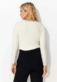 Haut blanc à manches longues à côtes, avec un col rond et une accent noir le long du col arrière, associé à un pantalon noir taille haute.