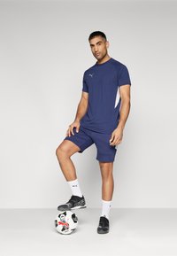 Marineblauwe sportt-shirt en shorts, met een witte accent. Zwarte schoenen en witte sokken. Zwart-witte voetbal met grafisch ontwerp.