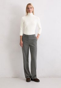 Witte coltrui, grijze krijtstreepbroek, relaxed fit, gladde textuur, met zijzakken, gedragen met bruine instappers.