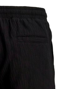Gros plan sur un short en tissu noir texturé avec une ceinture élastique et une seule poche passepoilée à l'arrière.