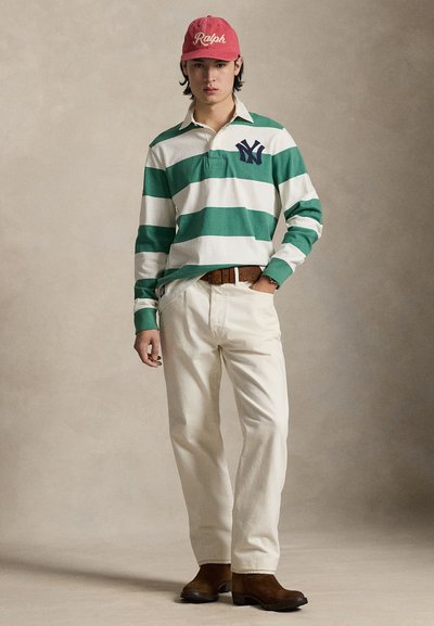 Roheliste ja valgete triipudega pikkade varrukatega polo särk tikitud logoga, kreemjad püksid, pruunid kontsakingad ja roosa nokamüts tekstifiguuriga.