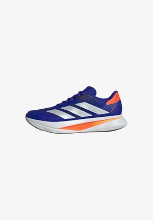 Sapatilha atlética roxa com riscas prateadas e um detalhe laranja. Design leve, com parte superior em malha e sola acolchoada.