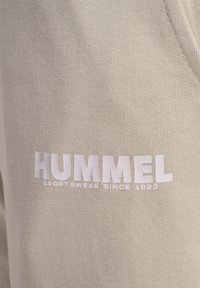 Beżowy sweatshirt z teksturowanej tkaniny, z wyraźnym białym logo "HUMMEL" oraz napisem "SPORTSWEAR SINCE 1923" w kontrastowym druku.
