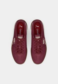 Bordowe sneakersy z teksturowaną cholewką, wyposażone w wyściełane kołnierze, sznurówki i gumową podeszwę. Detale logo na języku i etykiecie bocznej.