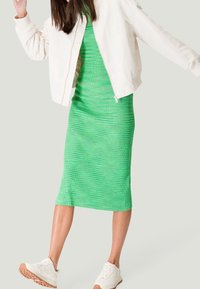 Robe midi côtelée verte associée à une veste bomber crème et des baskets blanches. La robe est ajustée et présente une finition texturée.