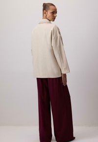 Beżowa oversizeowa kurtka z kołnierzem, szczegółowym przeszyciem i długimi rękawami. W połączeniu z szerokimi bordowymi spodniami. Gładka faktura, minimalistyczny design.