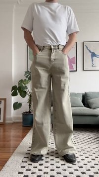 Lichtbeige wijde jeans met een hoge taille, textuurstof en zijzakken, gecombineerd met een simpel wit t-shirt en zwarte schoenen.