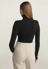 Czarny dopasowany sweter z wysokim kołnierzem i długimi rękawami, zestawiony z jasnobeżowymi spodniami o podwyższonej talii z przodu z plisa.