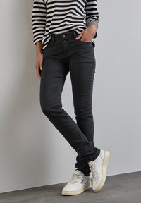 Svarta slim-fit jeans med fem fickor, knappstängning och subtila blekningar. I kombination med en svart och vit randig långärmad topp och vita sneakers.