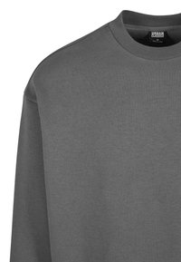 Felpa grigia con collo a giro, realizzata in morbido tessuto di cotone misto. Presenta polsini e fondo a coste, una texture sottile e nessuna grafica visibile.