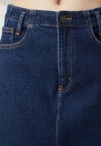 Jeanskjol i mörkblått med orange sömmar. Funktioner inkluderar hög midja, framfickor och knäppning med knapp. Mjuk textur, klassisk design.