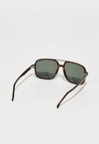 Bruine schildpad zonnebril met vierkante monturen, donkergroene glazen en slanke pootjes met subtiele metallic accenten.