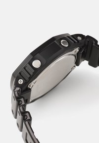 Black digital watch with a textured rubber band, metal accents, and a stainless steel back. Features buttons on the side for adjustments.