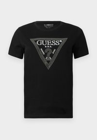 Black cotton t-shirt featuring a rhinestone triangle design with "GUESS" and "U.S.A." text, round neck, and short sleeves.