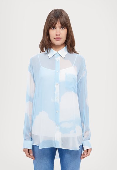 Blouse légère bleu clair avec des motifs de nuages blancs, design col, fermeture à boutons sur le devant, poche poitrine et manches longues avec poignets boutonnés.