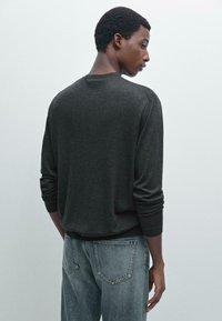 Dunkelgrauer Pullover mit langen Ärmeln und Rundhalsausschnitt, aus einem weichen Material gefertigt. Kombiniert mit hellblauen Jeans aus Denim mit Gesäßtaschen.